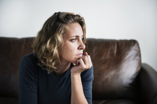 nervous woman staring out of the window while sitting on a brown couch