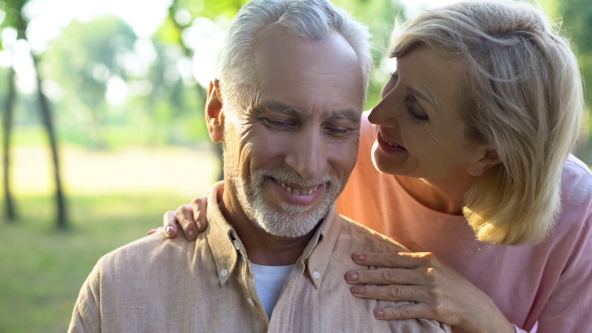 older white woman whispering to older white man outdoors