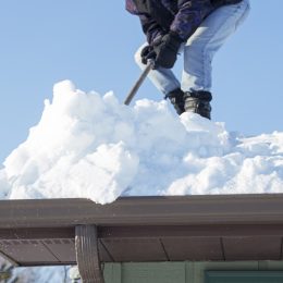 man scraping snow off roof