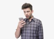 Close-up portrait of shocked young man looking at smart phone's screen receiving bad news on a white background