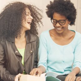 two women smiling while ready a book together