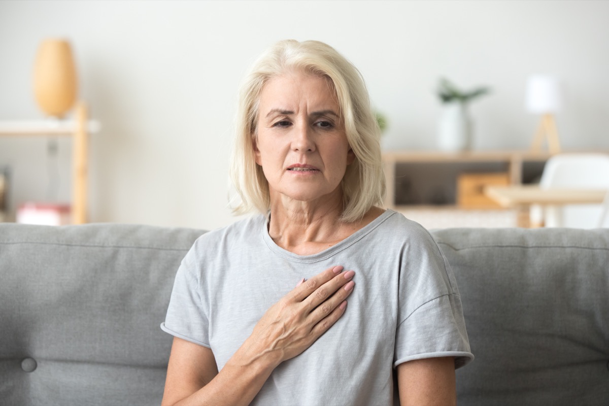 Middle-aged woman clutching her chest in pain on the couch