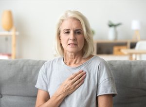 Middle-aged woman clutching her chest in pain on the couch