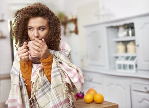 woman with red curly hair drinking from mug while wearing blanket