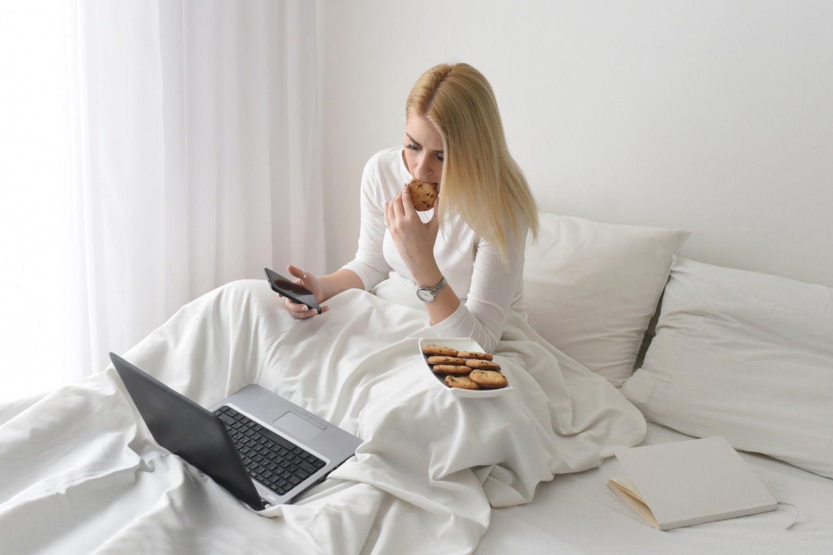 Woman eating cookies in bed with a laptop