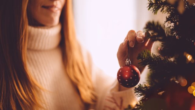 woman hanging red christmas ornament on her christmas tree