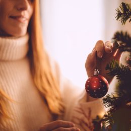 woman hanging red christmas ornament on her christmas tree