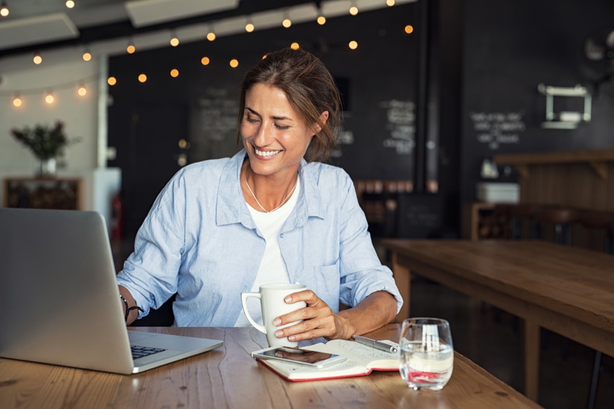 Woman happy and smiling while working on a laptop from a cafe