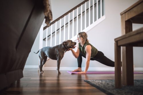 Femeie făcând exerciții fizice și făcând lungi cu câinele ei în camera de zi