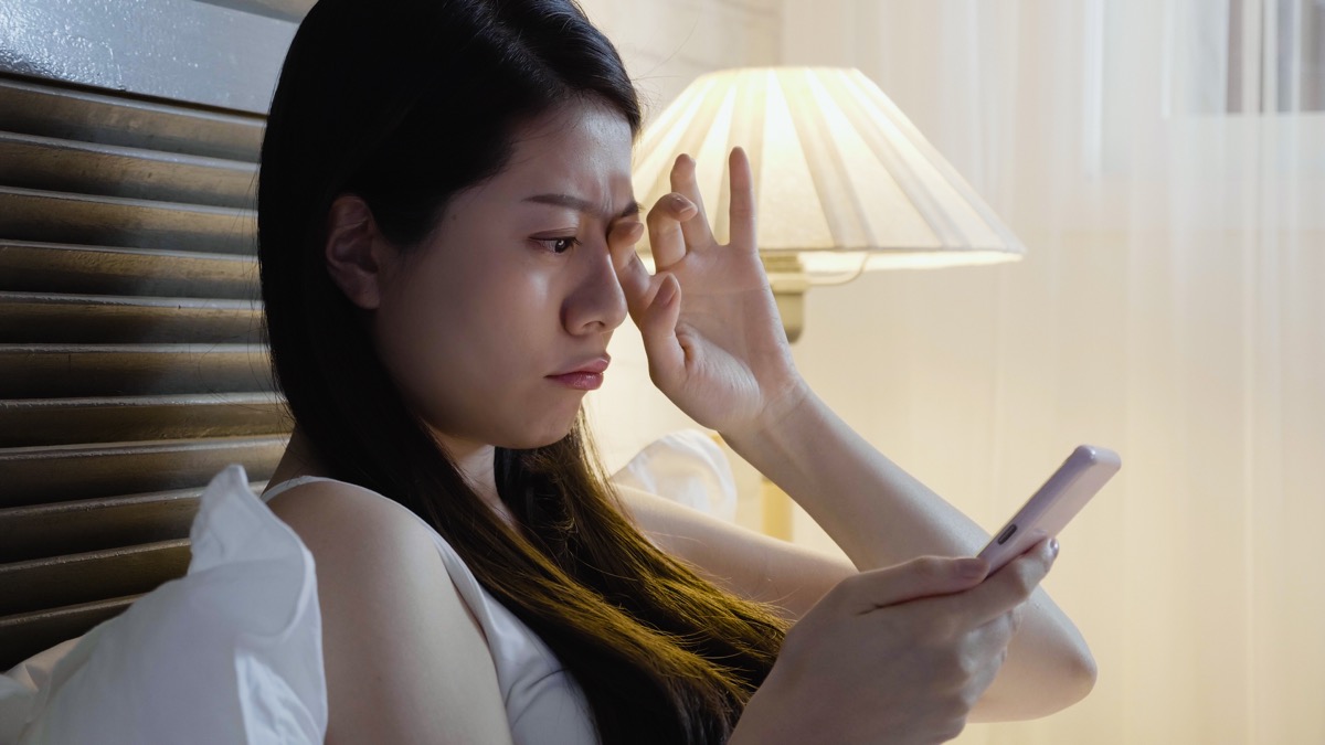 Woman rubbing her eyes in pain because she is using her cell phone
