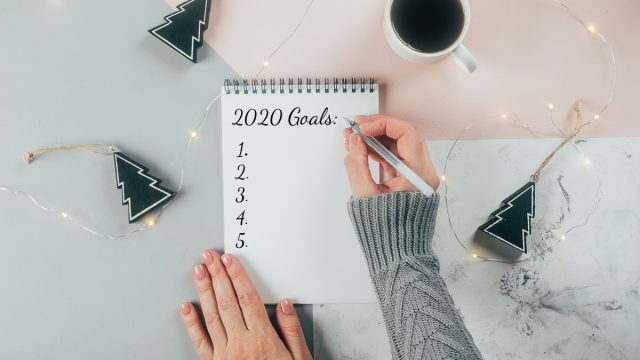 white hand writing down 2020 goals in notebook
