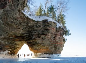 people walking underneath the rock formation on one of the apostle islands