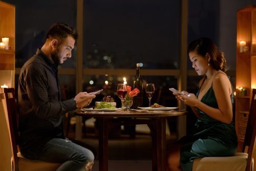 white man and asian woman on phone at dinner