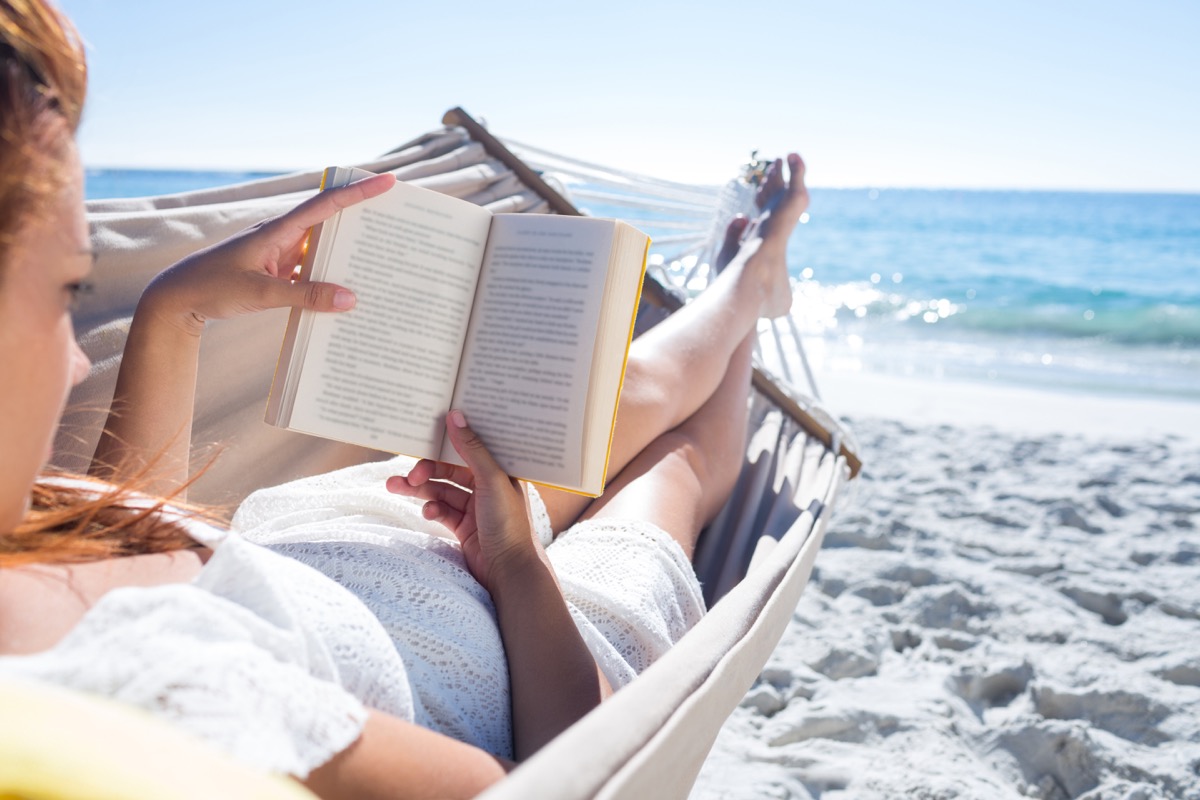 Woman reading a book in a hammock on the beach