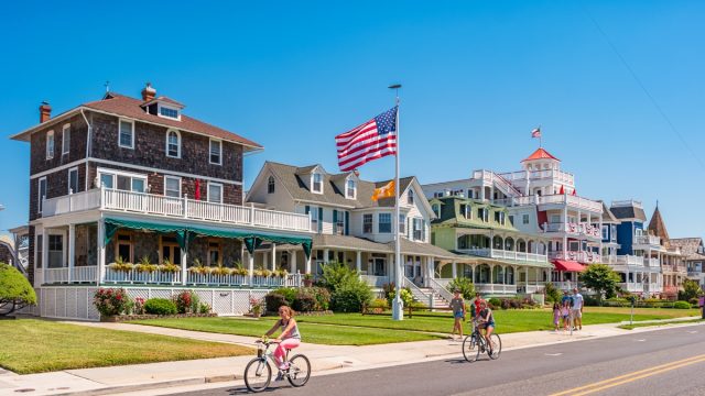People bike and walk in front of traditional villas in Cape May, New Jersey, USA, on a sunny summer day.