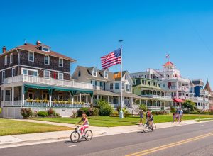 People bike and walk in front of traditional villas in Cape May, New Jersey, USA, on a sunny summer day.