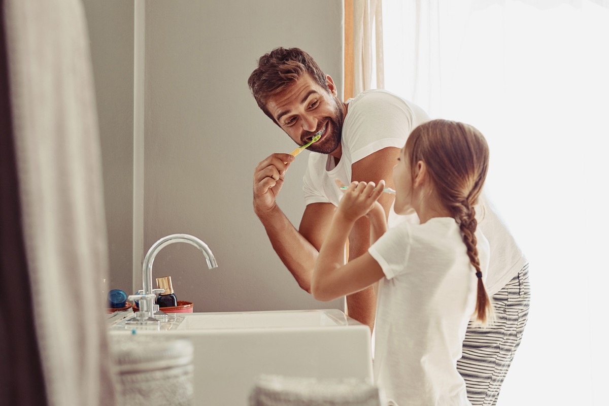 Happy father and his little girl brushing their teeth together in the bathroom