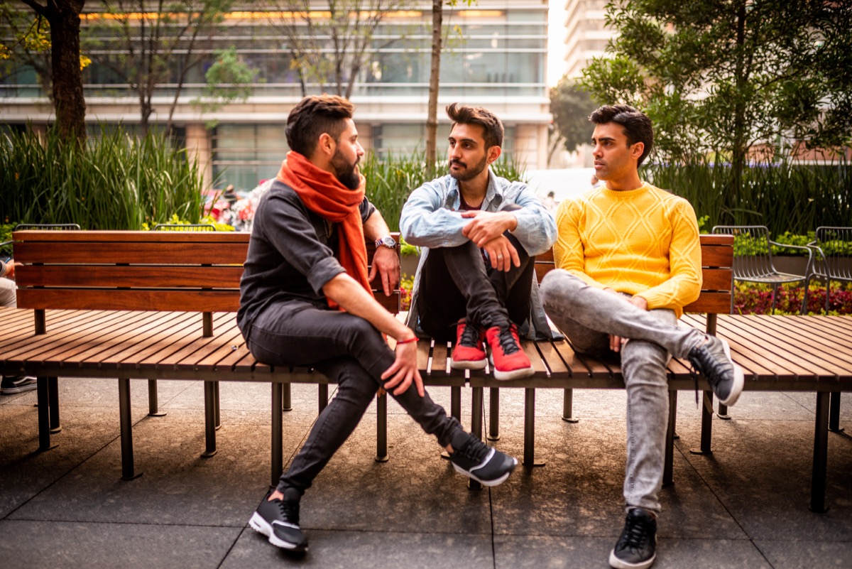 group of three male friends sitting on a bench in neighborhood