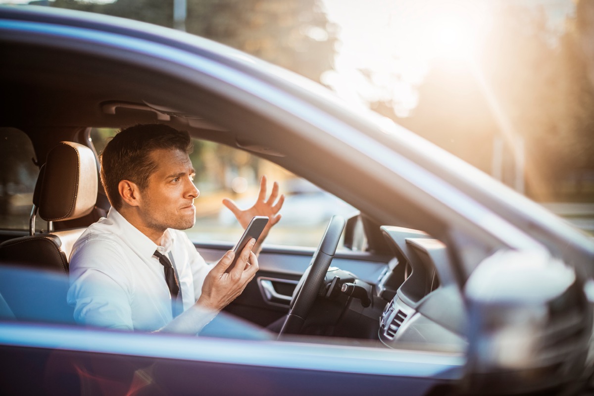 Close up photo of a businessman yelling at his phone while driving