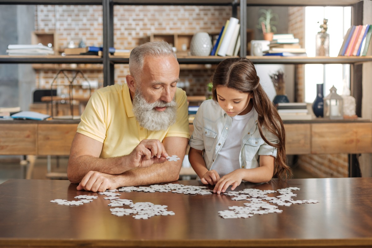 Grandfather and granddaughter doing a jigsaw puzzle together at the table