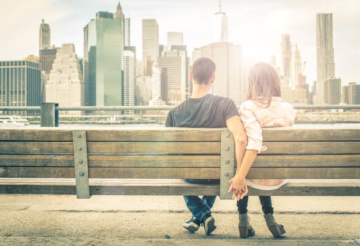 Couple holding hands on park bench looking at the city skyline