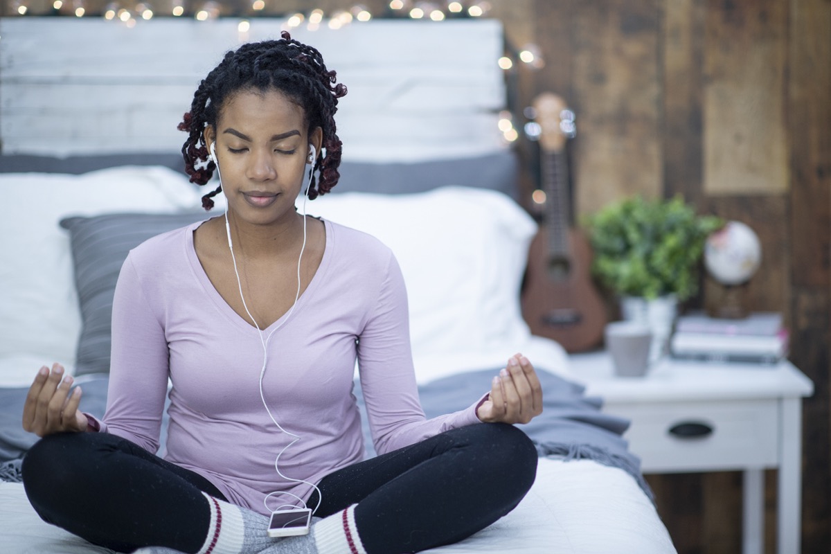 black woman meditating and listening to music on her bed
