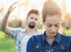 white woman looking sad with white man behind her throwing up his hand in anger