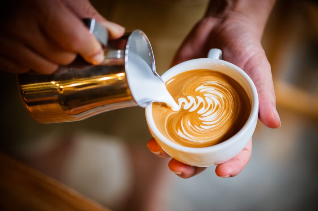 Barista making latte swirl art with golden creamer
