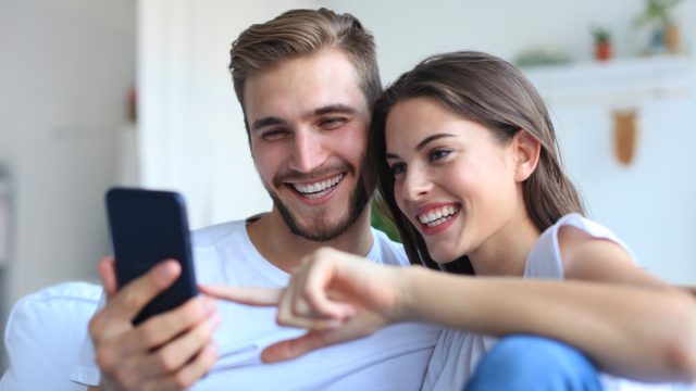 Couple looking and laughing at phone on couch