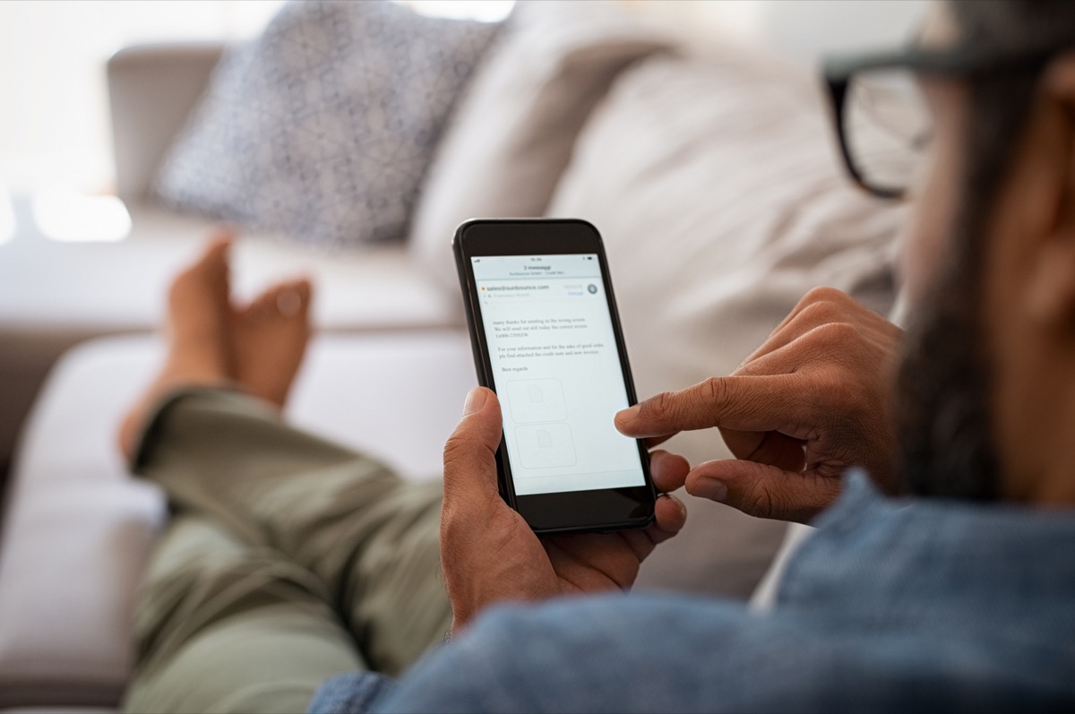 closeup of a man hand holding cellphone with internet browser on screen. Man with spectacles relaxing sitting on couch while looking at mobile phone. Closeup of mature latin man using smartphone to checking email at home