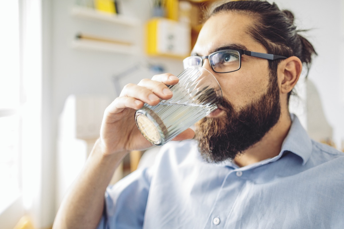 Man with a man bun and glasses drinking water at home