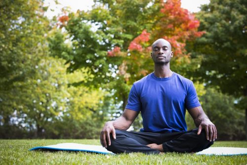 Man meditating during yoga outdoors on yoga mat