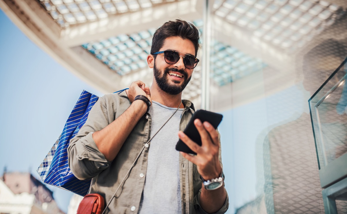 Man with shopping bags smiling at his phone