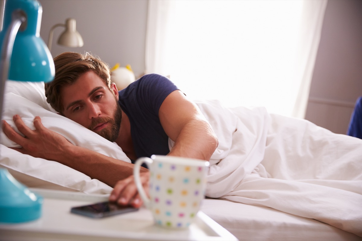 Man sleeping in waking up late in the morning checking phone