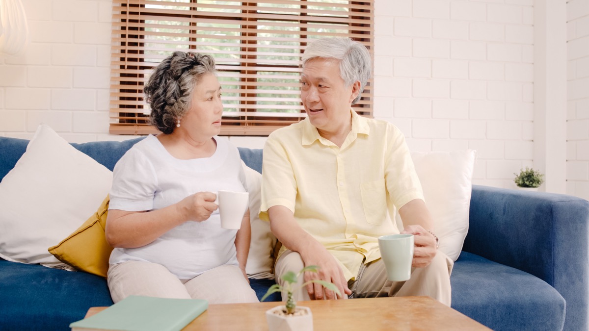 Older couple talking on the couch while drinking coffee or tea serious talk