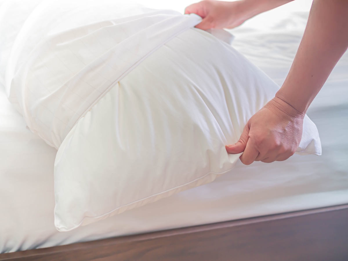 white pillow on the bed in the bedroom with woman 's hand who are making the room.
