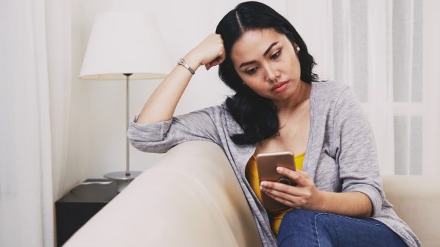 sad pensive young Filipino woman reading text messages or news on smartphone