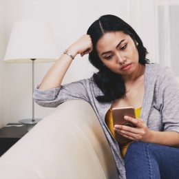 sad pensive young Filipino woman reading text messages or news on smartphone