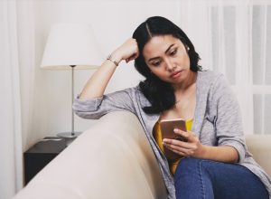 sad pensive young Filipino woman reading text messages or news on smartphone