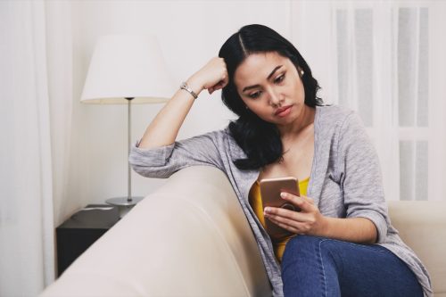 sad pensive young woman reading text messages or news on smartphone