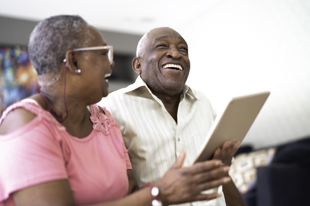 Senior black couple laughing while looking at tablet