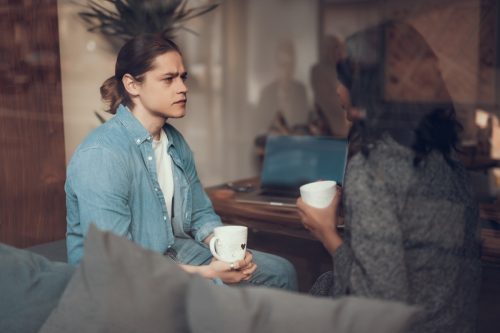 σοβαρή κουβέντα.  Συγκεντρωμένος νεαρός άνδρας κάθεται με ένα φλιτζάνι τσάι και συνοφρυώνεται ενώ ακούει προσεκτικά τη φίλη του και την κοιτάζει