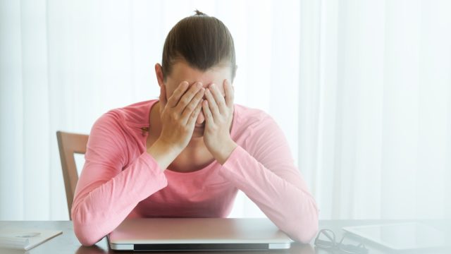 stressed out 30-something white woman sitting with face in hands over laptop