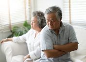 older asian couple sitting on couch looking upset and angry