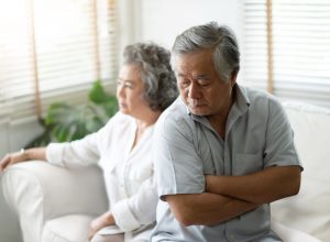 older asian couple sitting on couch looking upset and angry