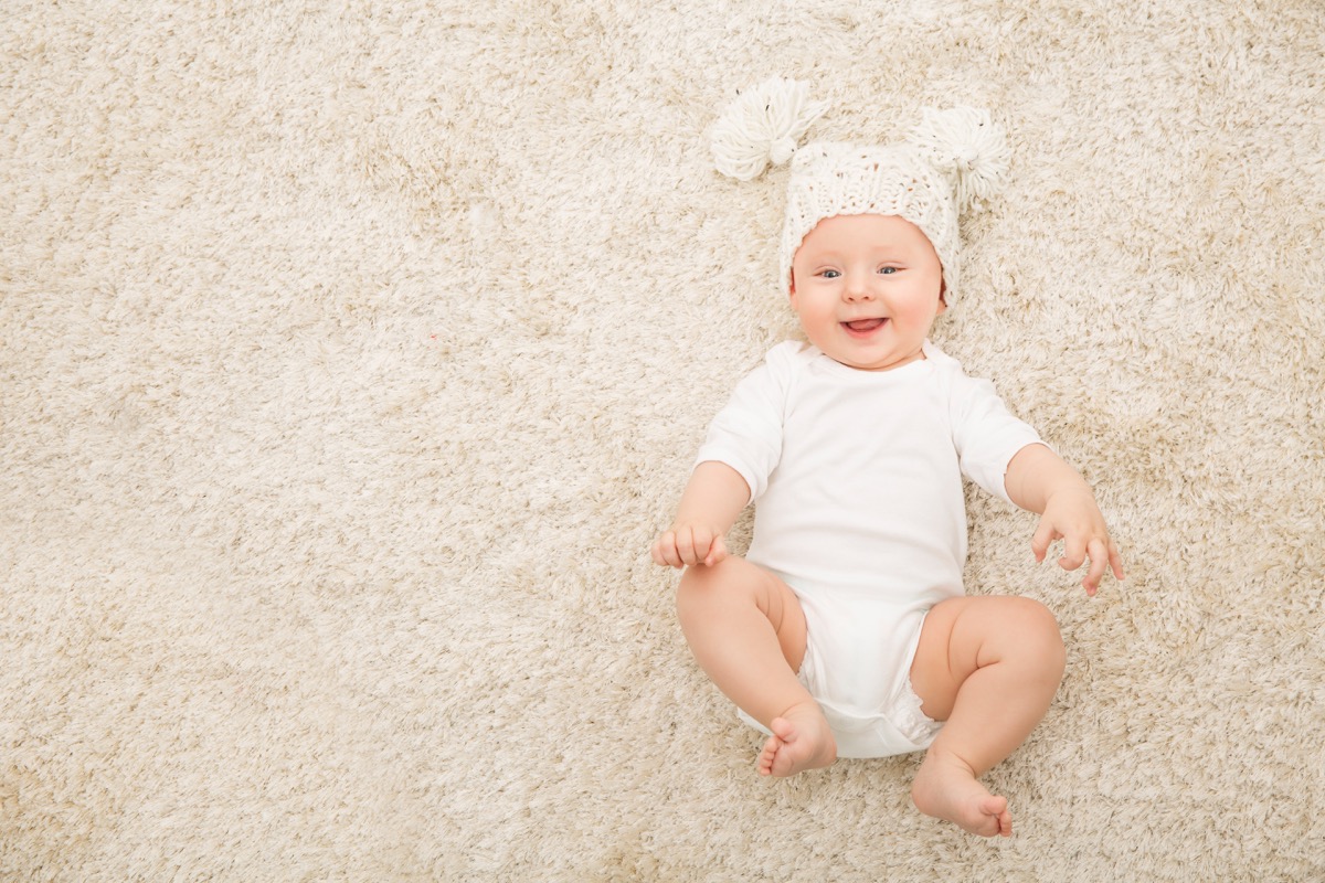 white baby wearing pom pom hat on rug