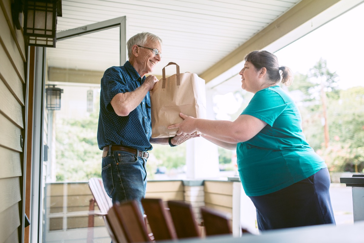 A kind and caring neighbor or friend delivers fresh produce from the grocery store to an elderly man at his home. 