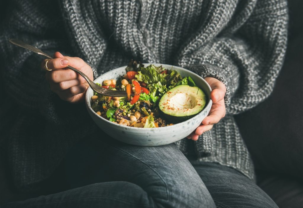 close up on woman in sweater eating a veggie and grain bowl