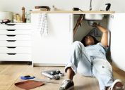 black woman laying down on floor fixing pipes under kitchen sink