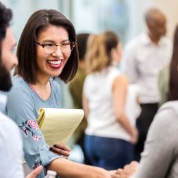 cheerful young businesswoman stands with an unrecognizable coworker in a crowded office building and smiles as she shakes hands with her new unrecognizable client